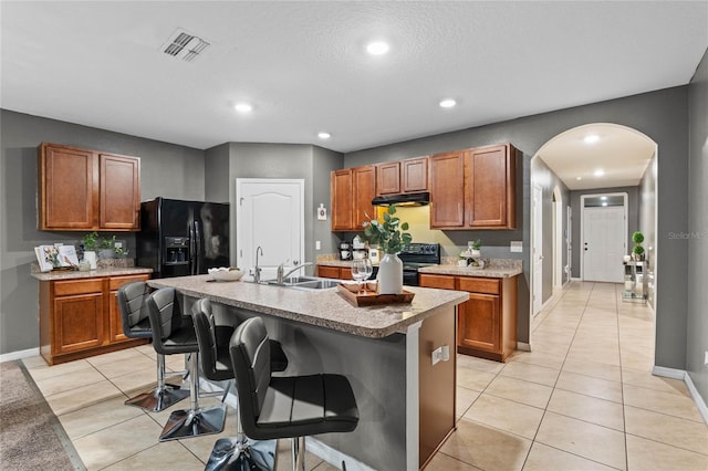 kitchen featuring light tile patterned floors, a kitchen bar, black appliances, and an island with sink