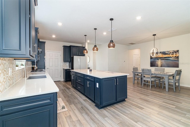 kitchen featuring a center island, white fridge, blue cabinetry, backsplash, and hanging light fixtures