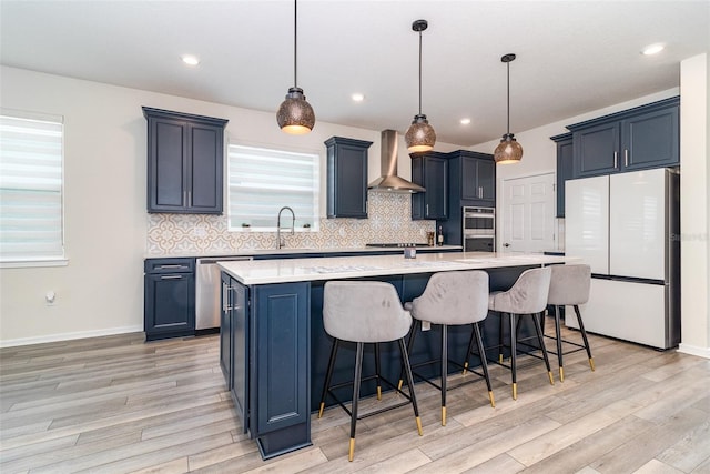 kitchen with decorative light fixtures, a spacious island, wall chimney range hood, and appliances with stainless steel finishes