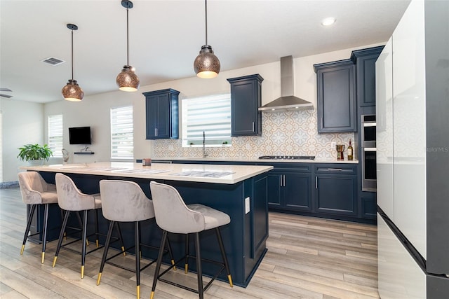 kitchen featuring pendant lighting, a center island, wall chimney exhaust hood, a breakfast bar, and gas cooktop