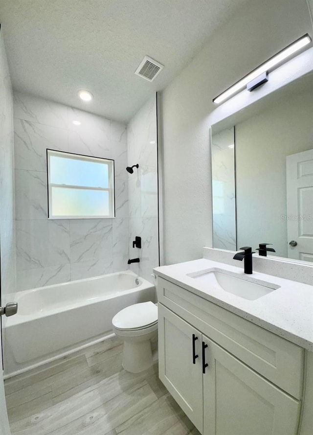 full bathroom with a textured ceiling, hardwood / wood-style floors, tiled shower / bath, vanity, and toilet