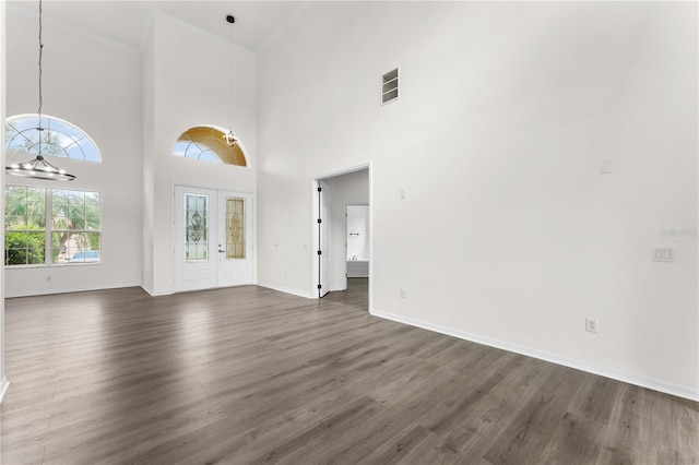 unfurnished living room with dark hardwood / wood-style flooring, a towering ceiling, french doors, and a chandelier