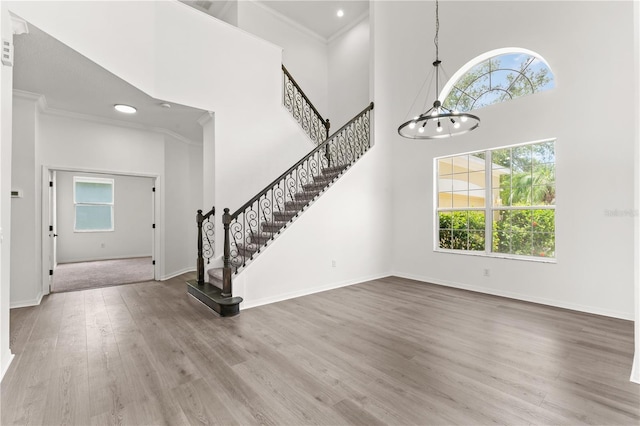 foyer entrance with hardwood / wood-style floors, a towering ceiling, crown molding, and a chandelier