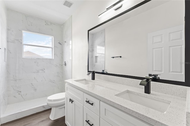 bathroom featuring a tile shower, vanity, hardwood / wood-style flooring, and toilet