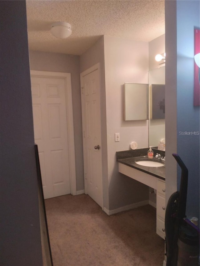 bathroom with a textured ceiling, a sink, and baseboards