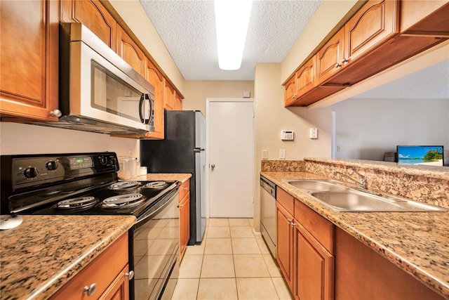 kitchen with light stone countertops, appliances with stainless steel finishes, a textured ceiling, sink, and light tile patterned flooring