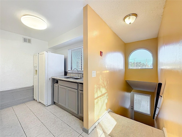 kitchen featuring a textured ceiling, gray cabinets, light tile patterned floors, and sink