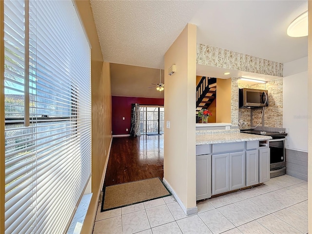 kitchen with ceiling fan, gray cabinets, a textured ceiling, appliances with stainless steel finishes, and light tile patterned flooring