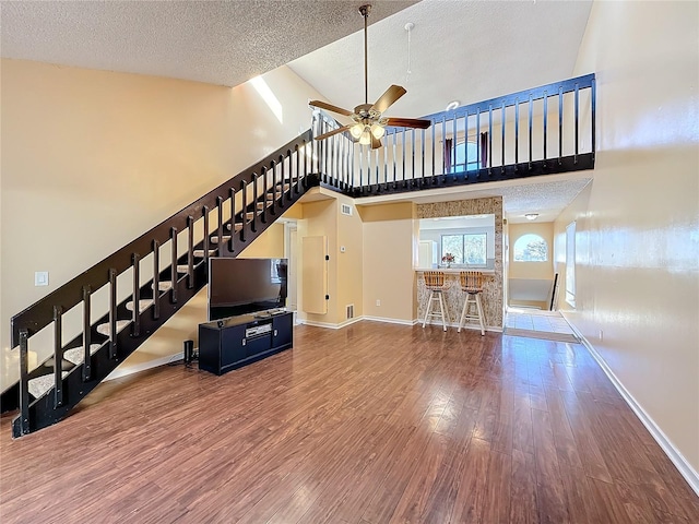 unfurnished living room featuring a textured ceiling, ceiling fan, hardwood / wood-style flooring, high vaulted ceiling, and bar area