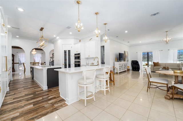 kitchen with sink, stainless steel double oven, a spacious island, decorative light fixtures, and white cabinets