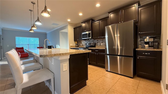 kitchen featuring appliances with stainless steel finishes, tasteful backsplash, a breakfast bar, a kitchen island with sink, and hanging light fixtures