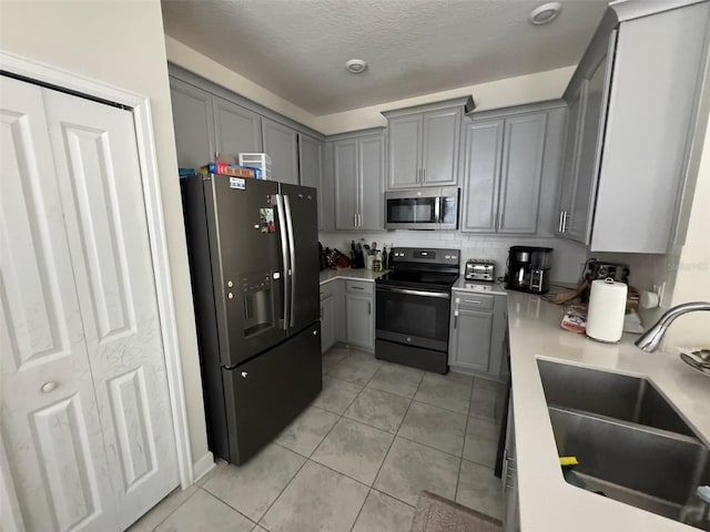 kitchen with light tile patterned floors, sink, appliances with stainless steel finishes, and gray cabinetry