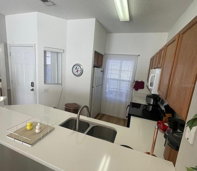 kitchen featuring kitchen peninsula, a textured ceiling, white appliances, and sink