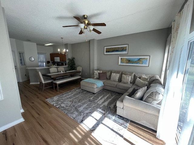 living room featuring dark hardwood / wood-style flooring, ceiling fan with notable chandelier, and a textured ceiling