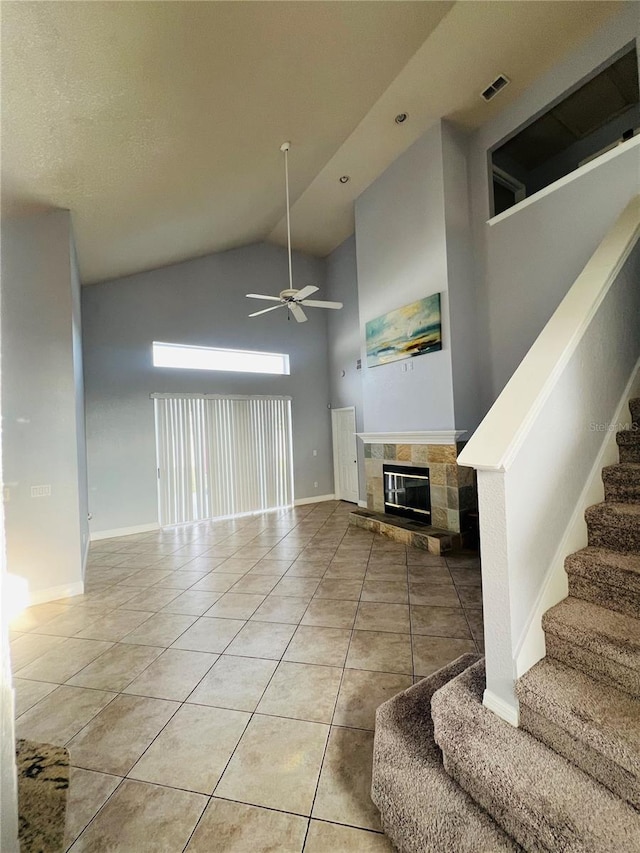 unfurnished living room with a tile fireplace, ceiling fan, a towering ceiling, and light tile patterned flooring