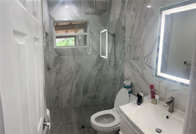 bathroom with toilet, a tile shower, vanity, and tile walls