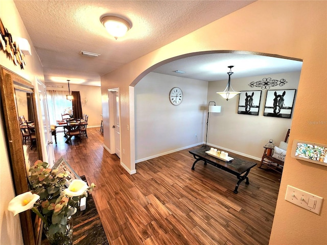 interior space with arched walkways, wood finished floors, baseboards, visible vents, and a textured ceiling
