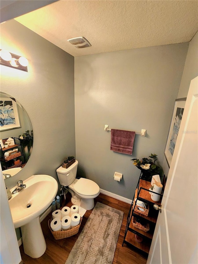 half bath featuring toilet, a textured ceiling, wood finished floors, and baseboards