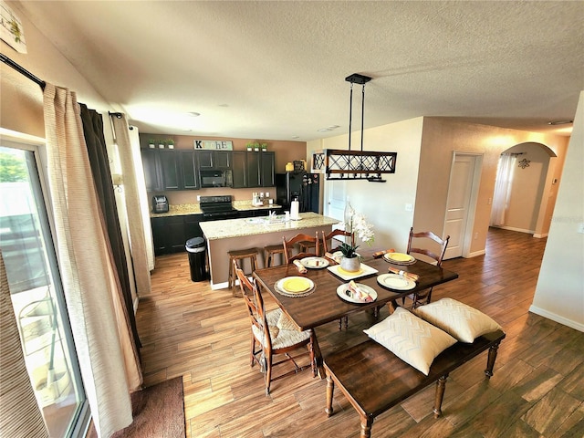 dining area with baseboards, wood finished floors, a textured ceiling, and arched walkways