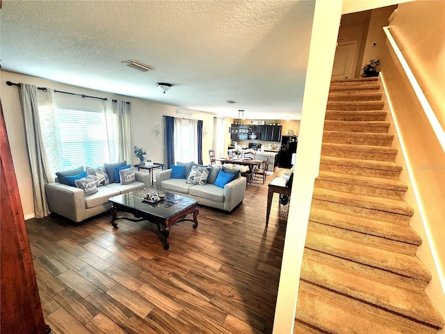 living room with a textured ceiling, visible vents, stairway, and dark wood finished floors