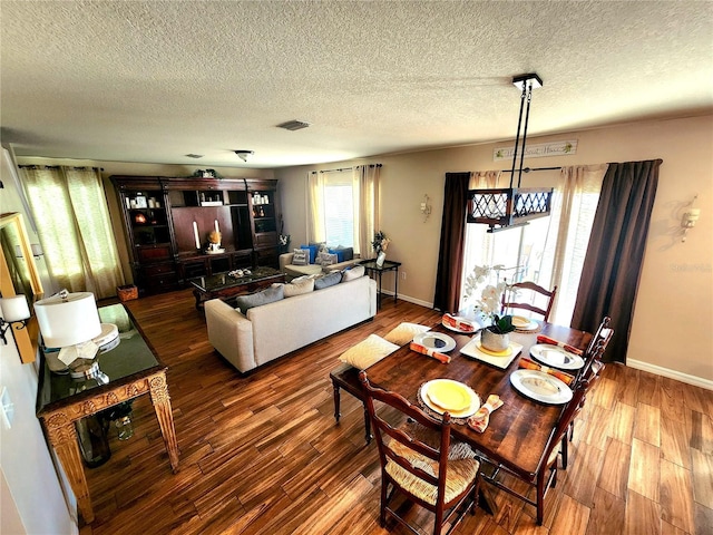 dining room featuring a textured ceiling, visible vents, a chandelier, baseboards, and wood finished floors