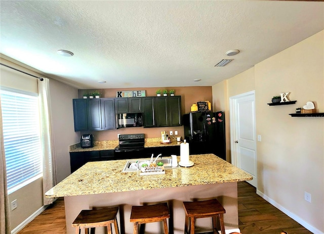 kitchen featuring a sink, black appliances, a kitchen breakfast bar, and visible vents