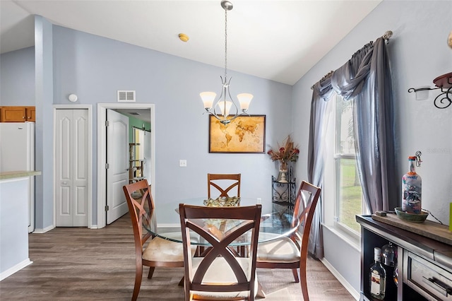 dining area with dark hardwood / wood-style flooring, vaulted ceiling, and an inviting chandelier