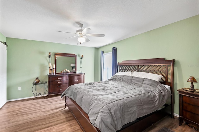 bedroom with a barn door, hardwood / wood-style floors, and ceiling fan