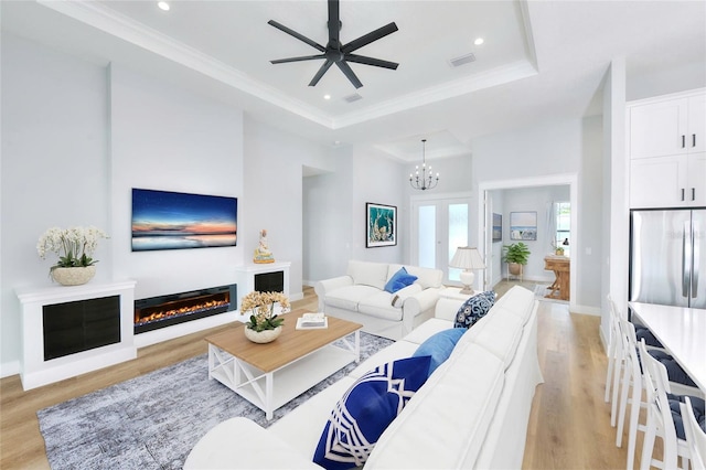 living room featuring ceiling fan with notable chandelier, light hardwood / wood-style flooring, a raised ceiling, and crown molding