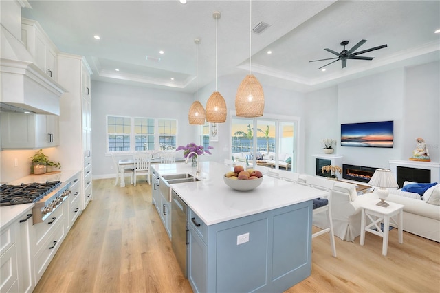 kitchen with pendant lighting, a kitchen island with sink, white cabinets, a raised ceiling, and appliances with stainless steel finishes