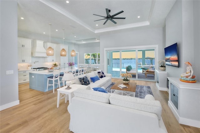 living room with ceiling fan, light wood-type flooring, a towering ceiling, and a tray ceiling