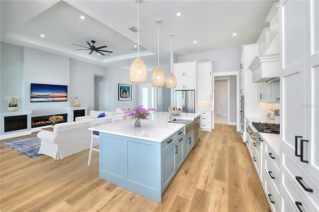 kitchen featuring a raised ceiling, sink, pendant lighting, white cabinets, and a large island