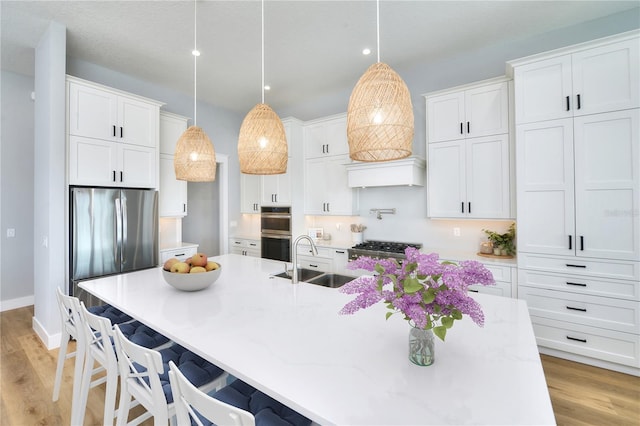 kitchen with appliances with stainless steel finishes, light wood-type flooring, sink, white cabinets, and hanging light fixtures