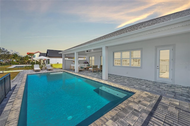 pool at dusk featuring outdoor lounge area, a patio, and ceiling fan