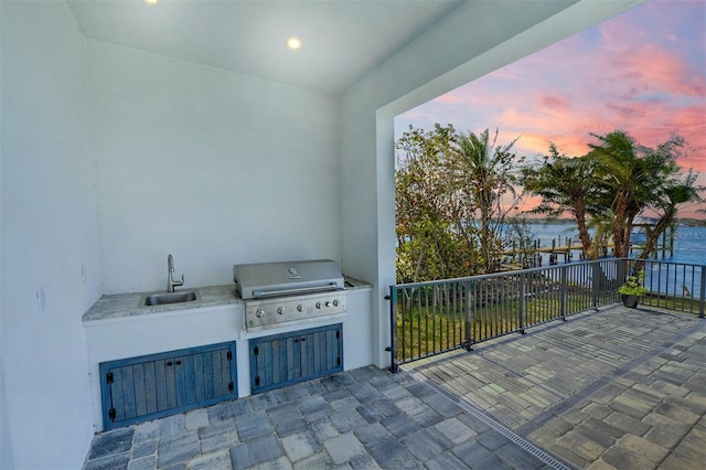 patio terrace at dusk featuring a grill, sink, a water view, and exterior kitchen