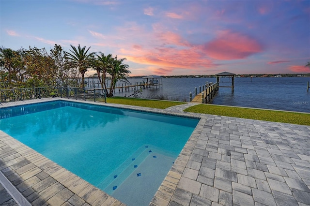 pool at dusk featuring a boat dock and a water view