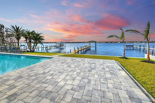 pool at dusk featuring a water view, a yard, and a dock