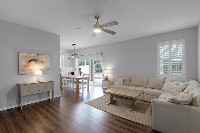 living room with dark hardwood / wood-style flooring, ceiling fan with notable chandelier, and a textured ceiling