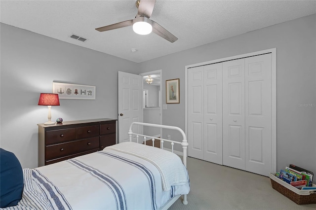 bedroom with ceiling fan, a textured ceiling, light carpet, and a closet