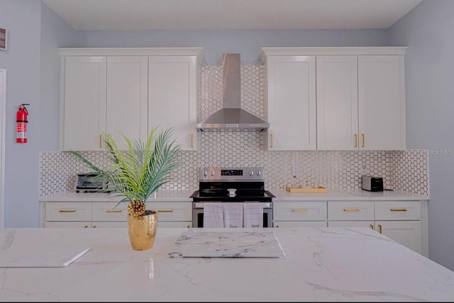 kitchen with stainless steel electric range, wall chimney exhaust hood, light stone counters, and white cabinetry