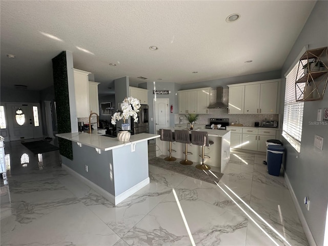 kitchen featuring white cabinetry, a kitchen bar, kitchen peninsula, backsplash, and wall chimney exhaust hood