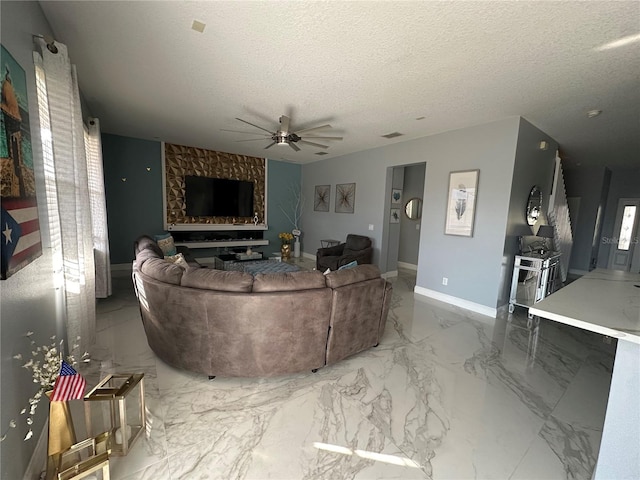 living room featuring ceiling fan, a textured ceiling, and a fireplace