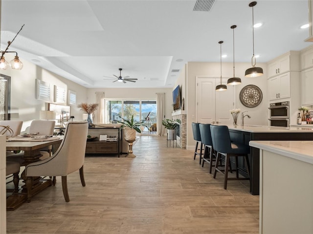 dining room featuring ceiling fan, sink, a raised ceiling, and light hardwood / wood-style floors