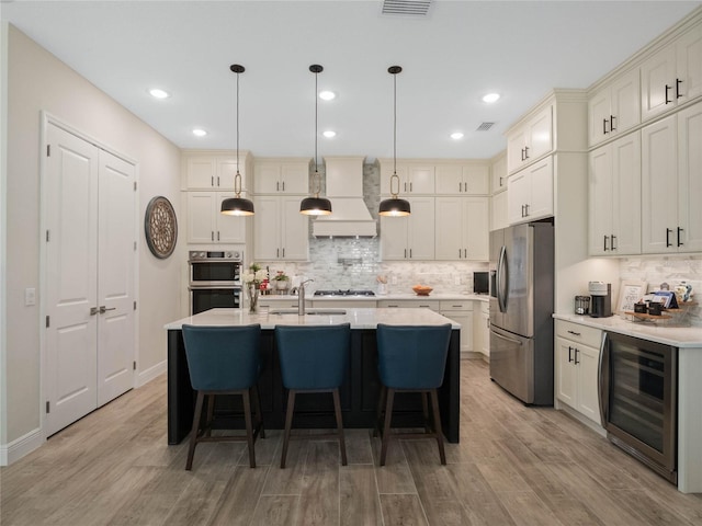 kitchen with wine cooler, hanging light fixtures, a kitchen island with sink, stainless steel appliances, and custom range hood