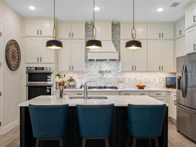 kitchen with light stone counters, stainless steel appliances, decorative light fixtures, and a center island with sink