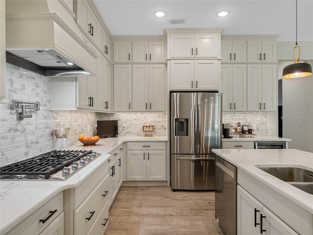 kitchen featuring appliances with stainless steel finishes, custom exhaust hood, hanging light fixtures, light hardwood / wood-style floors, and light stone countertops