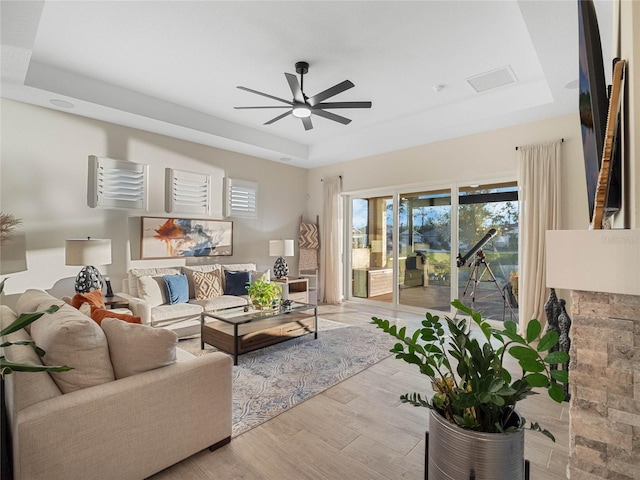 living room featuring ceiling fan, light wood-type flooring, and a tray ceiling