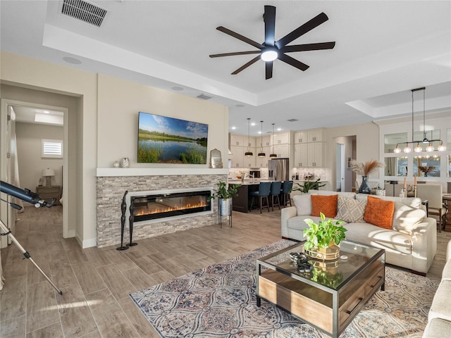 living room with a raised ceiling, a fireplace, and light hardwood / wood-style flooring