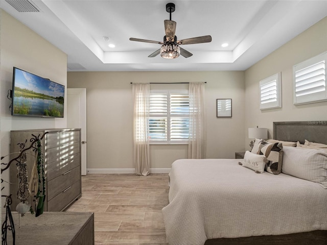 bedroom featuring a raised ceiling, ceiling fan, and light wood-type flooring