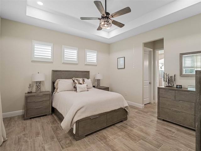 bedroom featuring ceiling fan, a tray ceiling, and light wood-type flooring